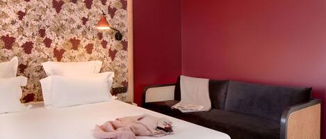 A hotel room with a bed, a dark sofa, and a wall with a floral pattern.