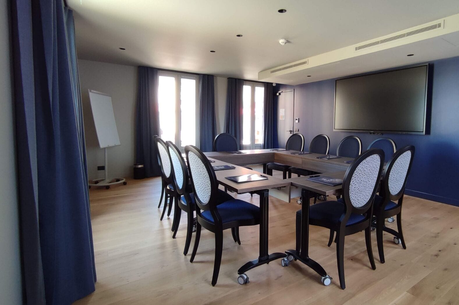 Ein Konferenzraum mit langem Tisch, sechs Stühlen, einer Projektionsleinwand und einer Whiteboard-Tafel.
