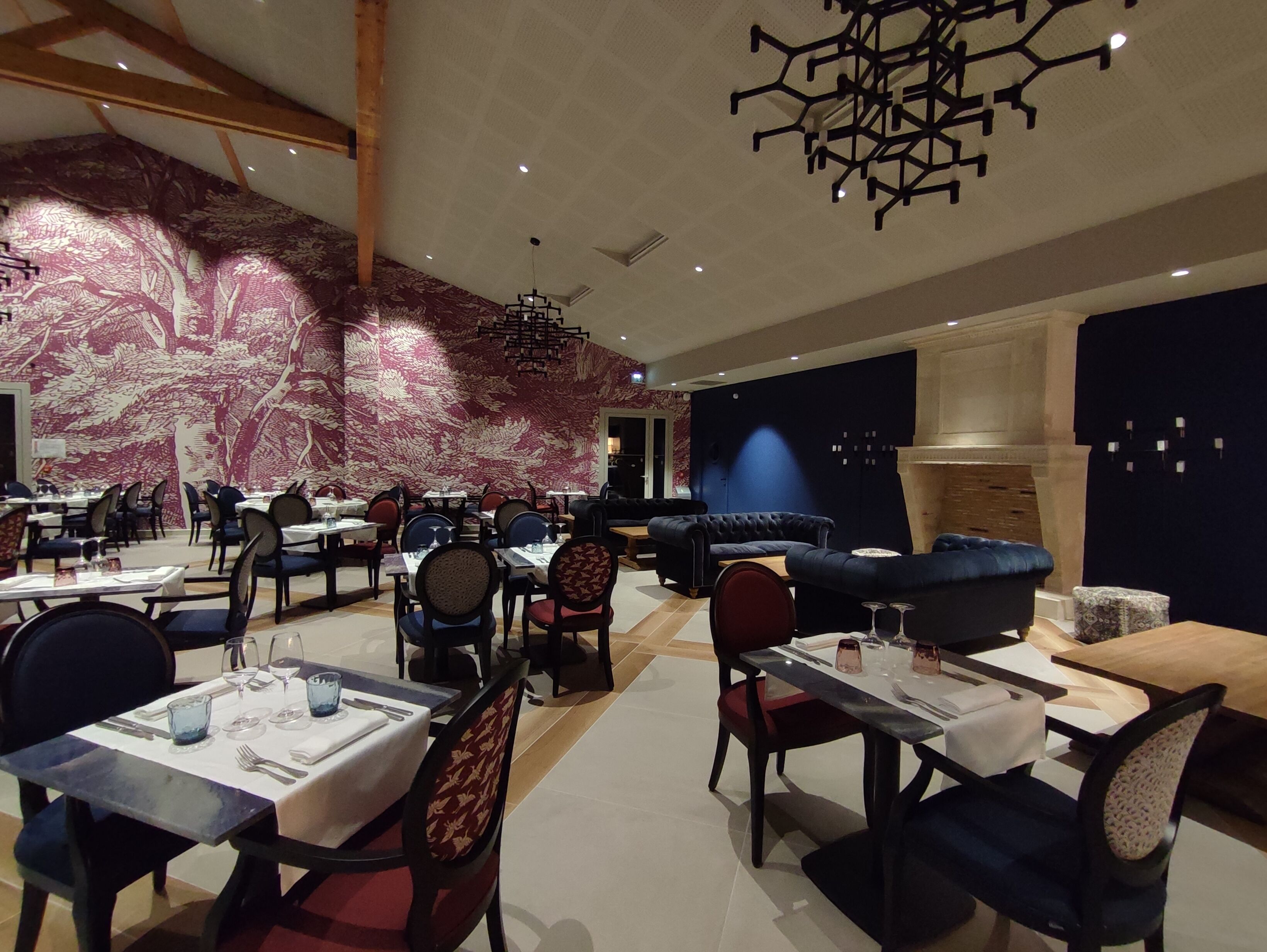 Un espace de restauration moderne, avec des tables et des chaises, un mur orné de motifs et un luminaire au plafond original.