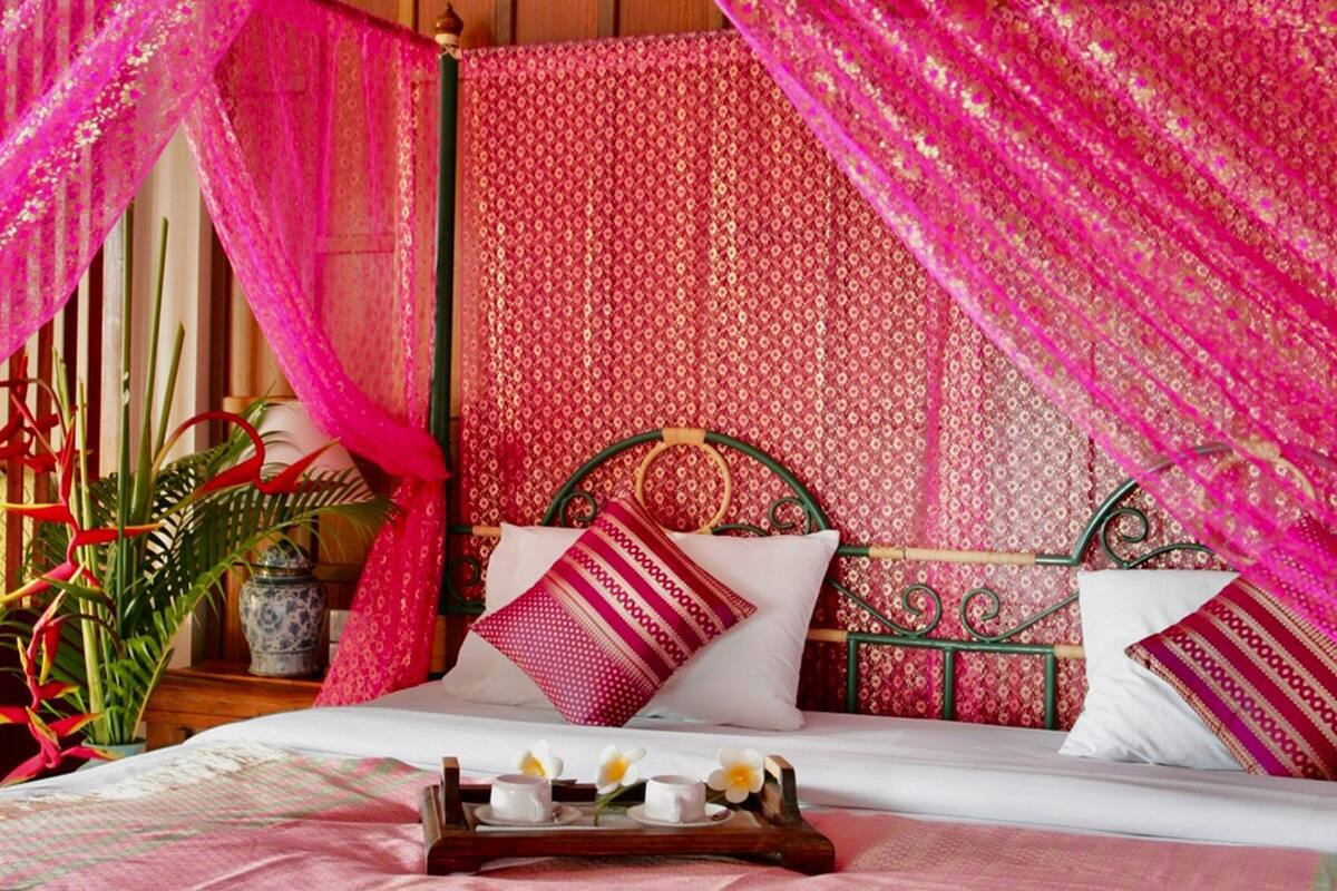 A bed with a canopy, pillows, a tray with cups, and a vase with flowers.