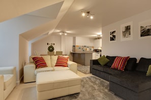 Relax in a spacious living area with a loft-style ceiling, featuring a sofa set, armchair, and ottoman.