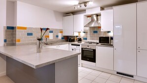 A modern kitchen with white cabinets, a central island, a microwave, an oven, and a gas stove. - BookedUK - Penthouse 3 Bedroom Apartment (Bishop's Stortford)