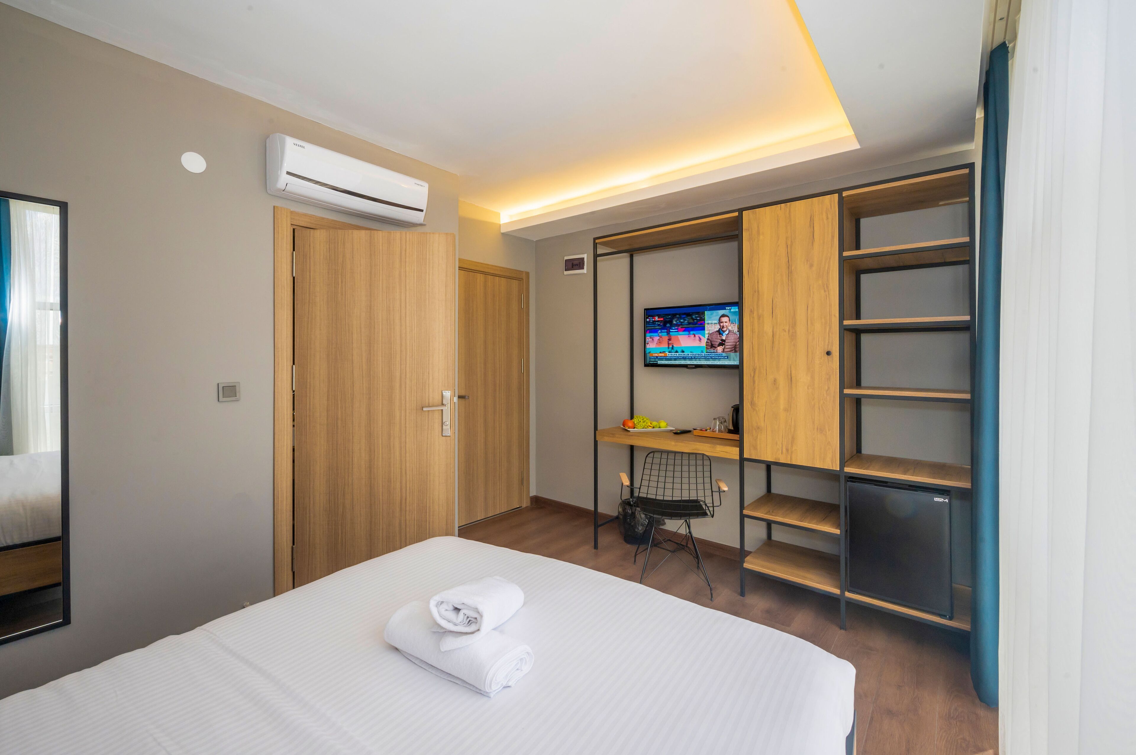 A hotel room with a bed, a TV, a wardrobe, and a desk with a chair.