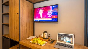 A hotel room with a wooden desk, a television displaying a news channel, a laptop, and a plate of fruit. - Corlu Dem Hotel (Corlu)