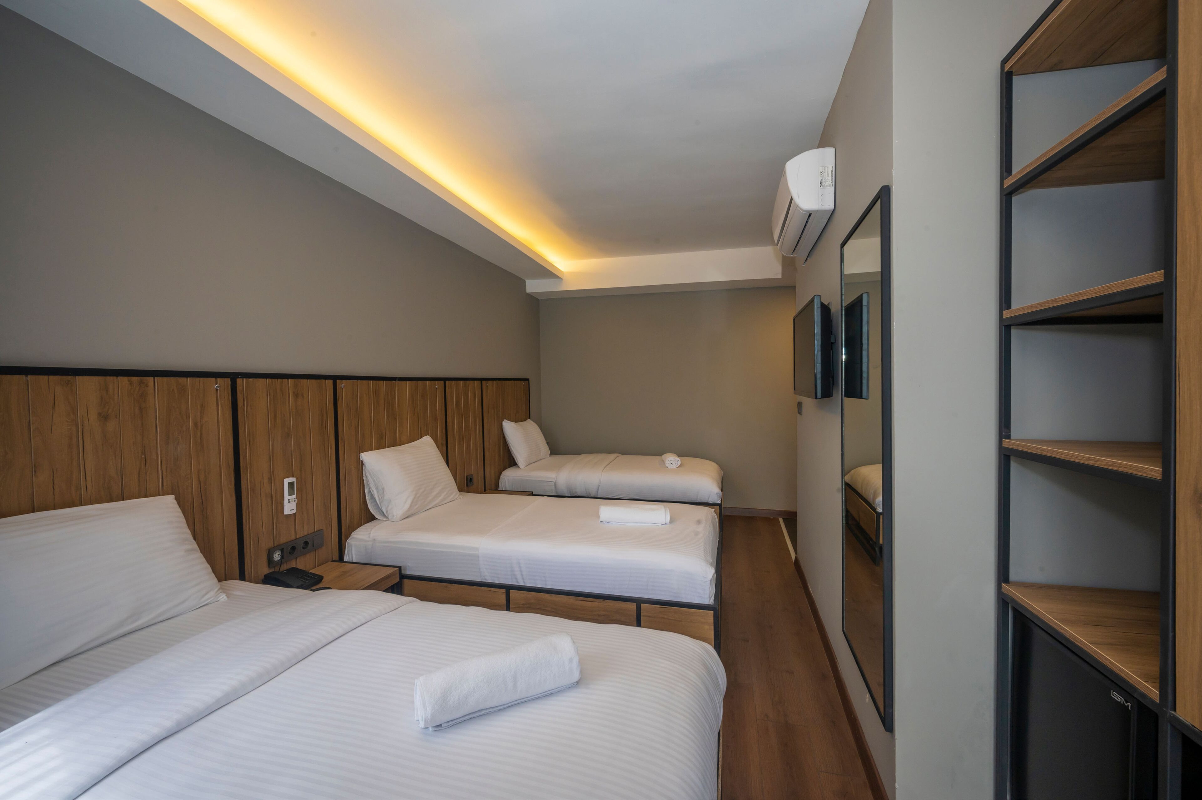 A hotel room with two beds, a wooden headboard, a bedside table with a phone, and a wall-mounted air conditioner.