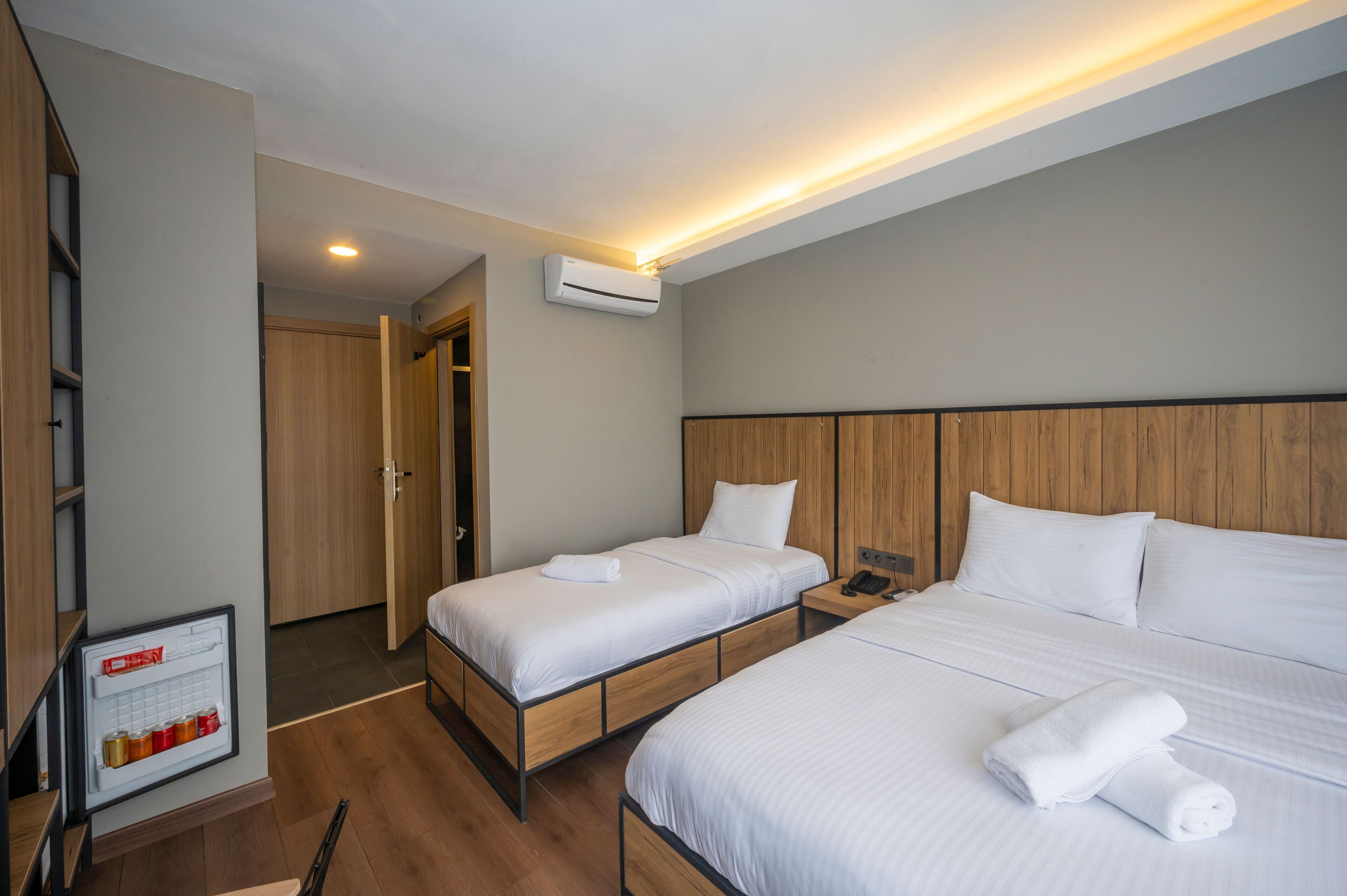 Habitación de hotel con dos camas, cabecera de madera, estante empotrado y aire acondicionado de pared.