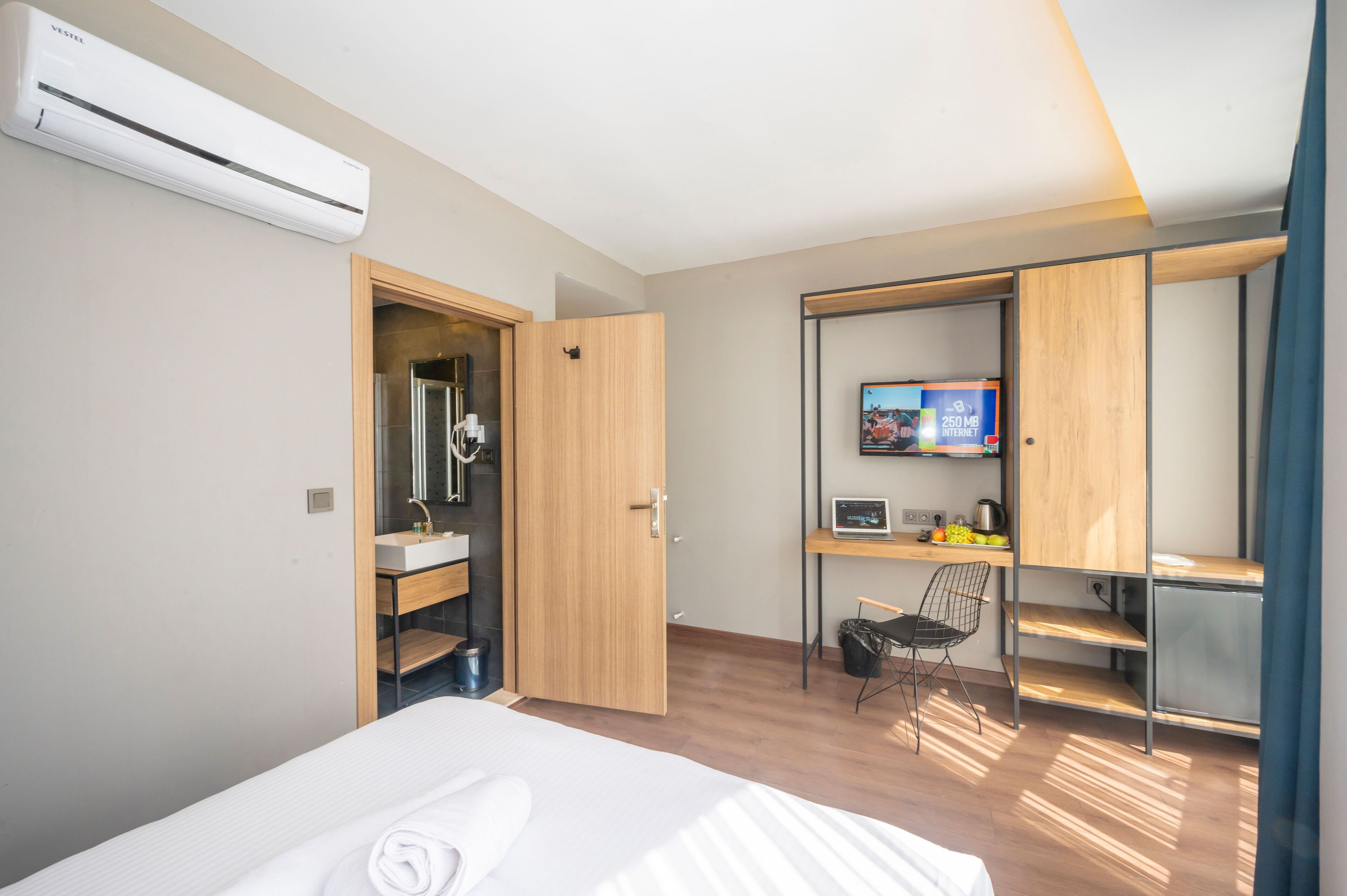 Een moderne hotelkamer met een bed, een badkamer met spiegel en wastafel, een bureau met computer en televisie, en een kledingkast.