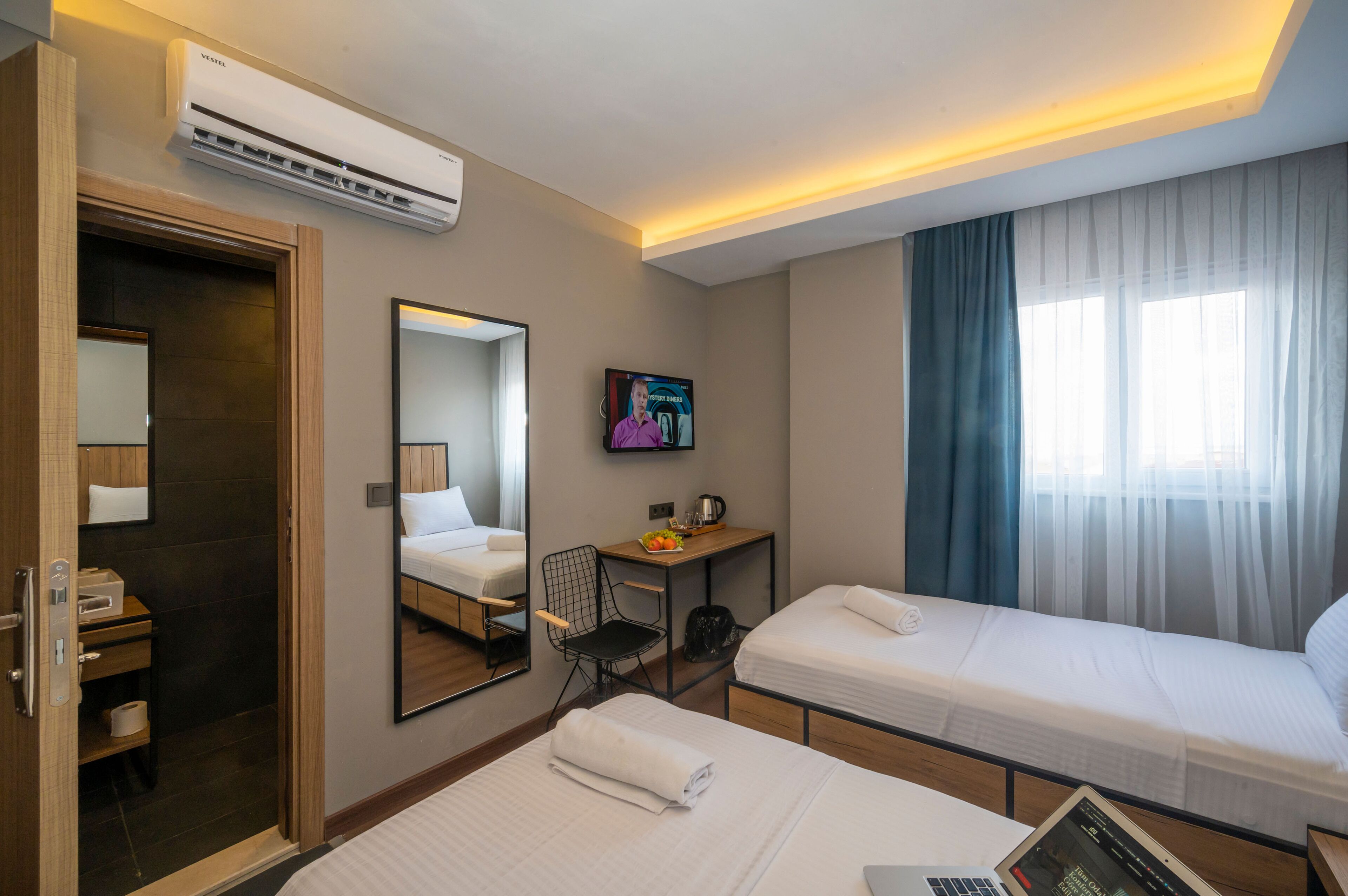 A hotel room with two beds, a desk with a chair, a TV, and a window with curtains.