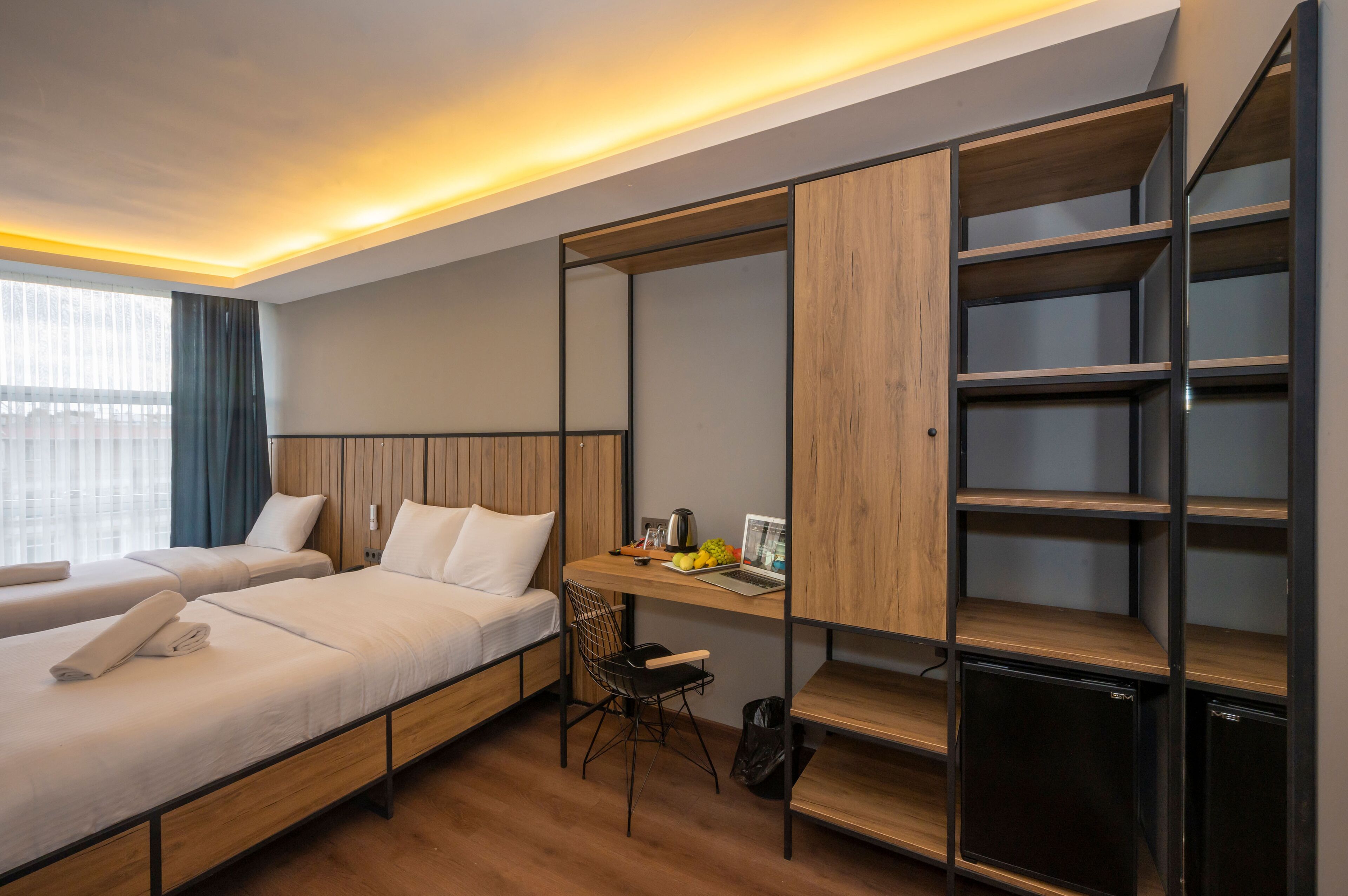A hotel room with two beds, a desk with a laptop, and built-in shelving.