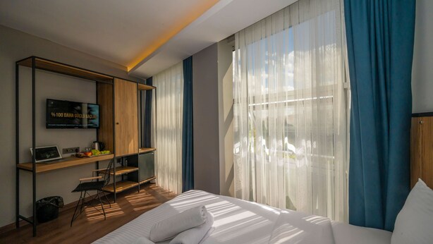 A modern hotel room with a bed, a desk with a laptop, and a TV on a wooden shelf. - Corlu Dem Hotel (Corlu)