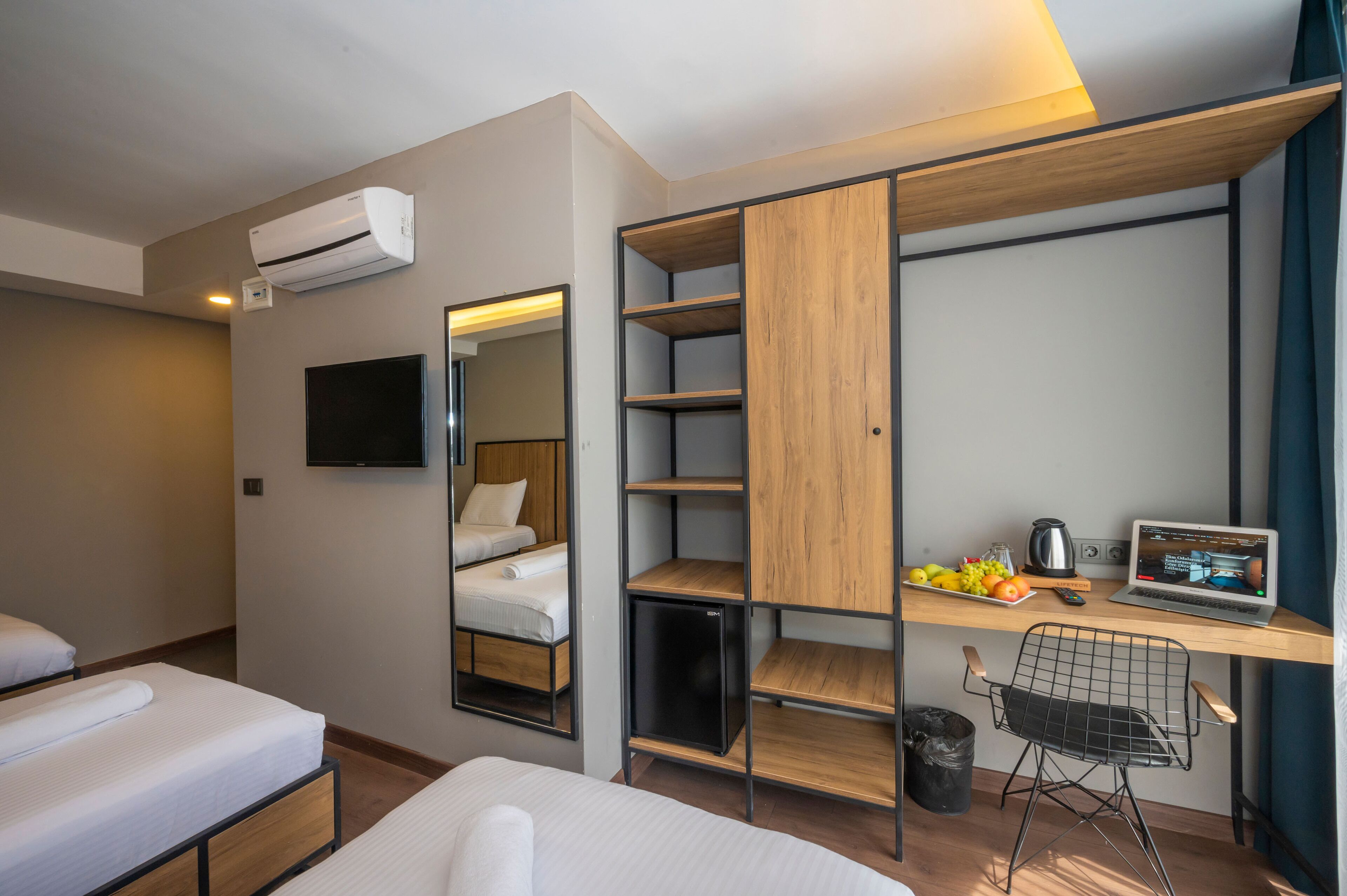 Quarto de hotel moderno com uma cama, uma escrivaninha com um laptop, um frigorífico pequeno e uma televisão.