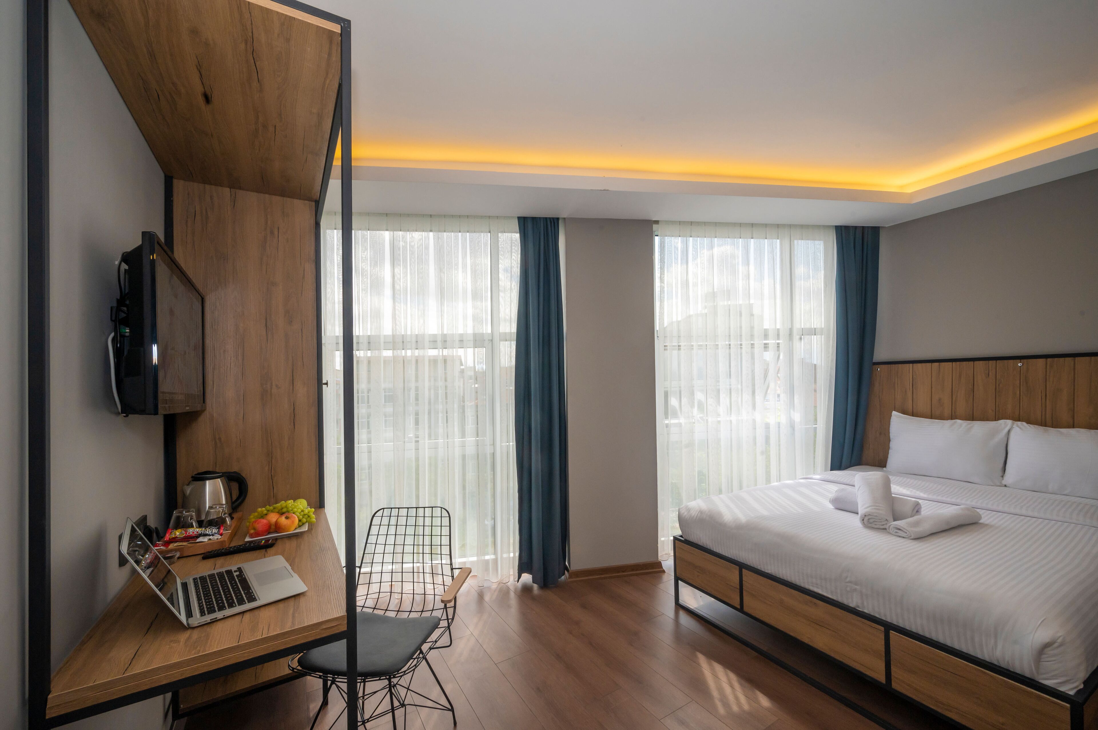 A modern hotel room with a wooden desk, laptop, and a bed with neatly folded towels.