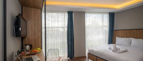 A modern hotel room with a wooden desk, laptop, and a bed with neatly folded towels.