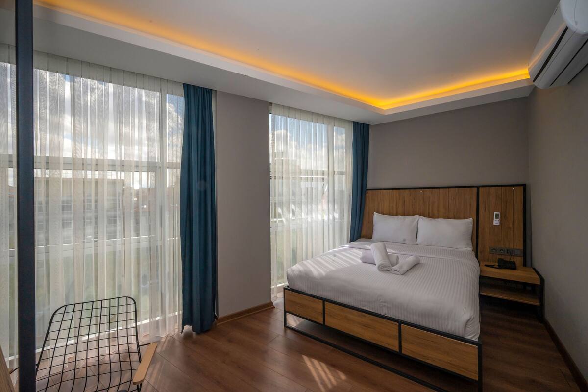 A modern hotel room with a large bed, a wooden nightstand, and a chair near the window.