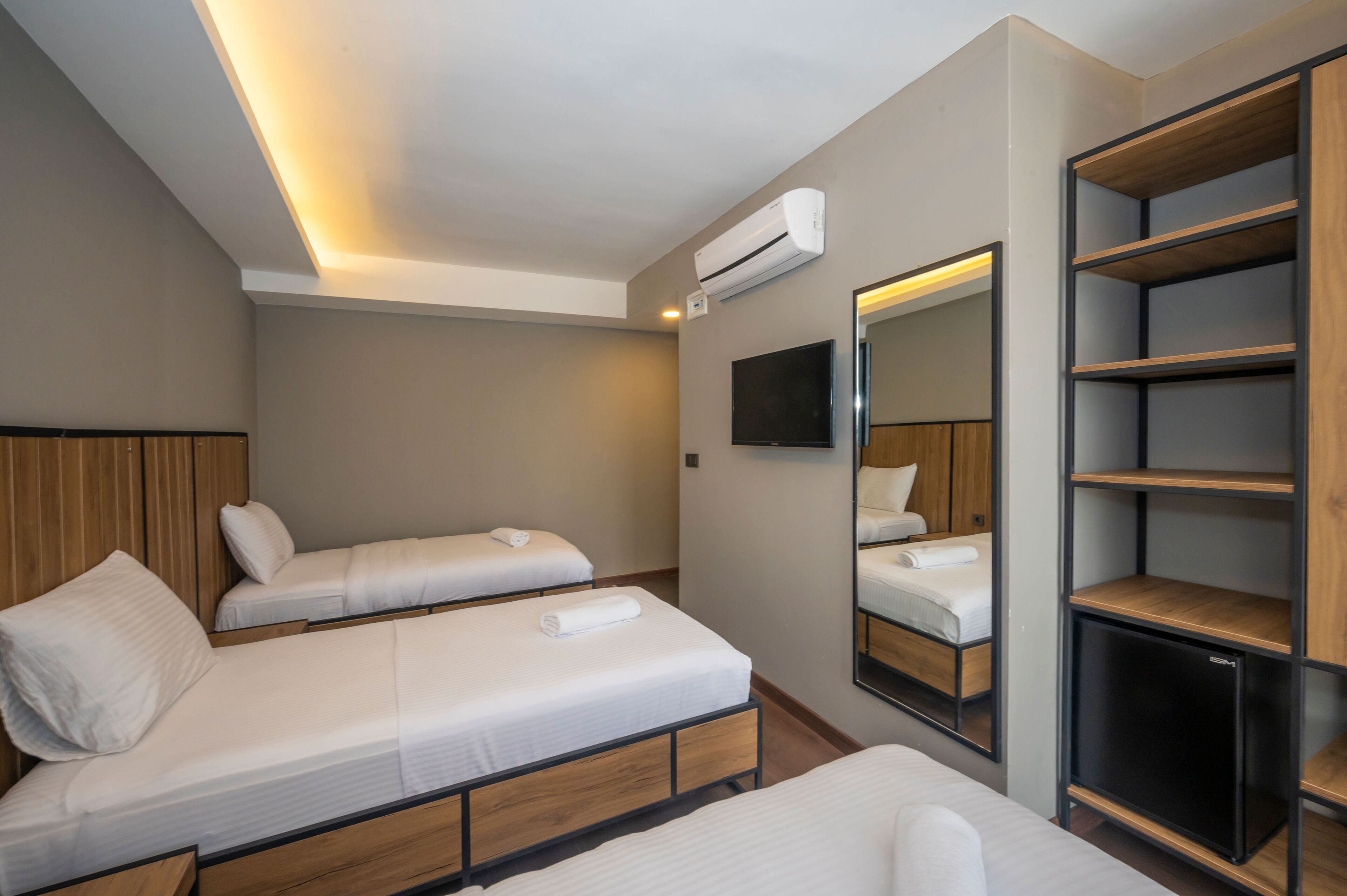 A hotel room with two single beds, a built-in TV, a wardrobe, and an air conditioning unit.