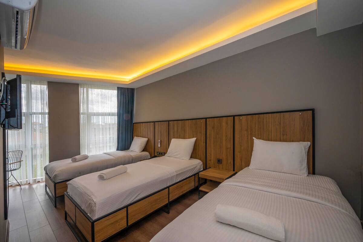 A hotel room with three single beds, a wooden headboard, a TV, and a window with curtains.