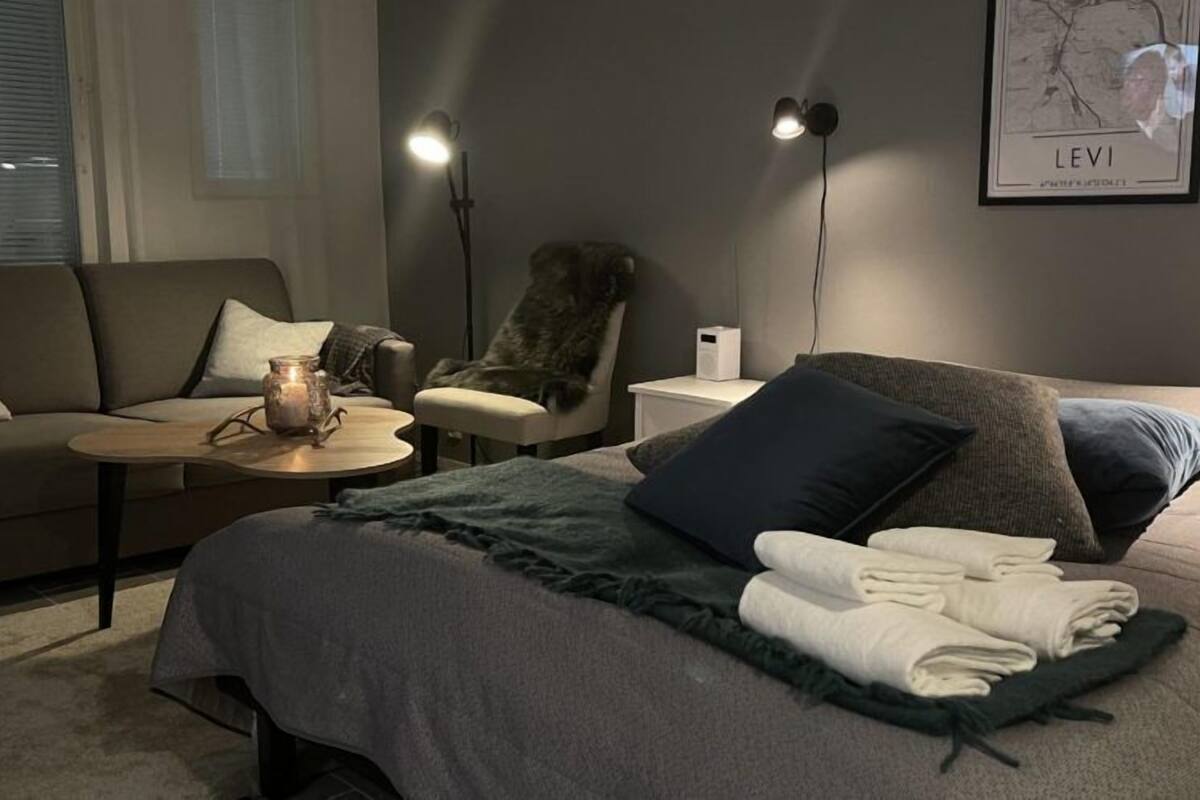 Un dormitorio moderno con cama, sofá, sillón, mesita y lámpara.