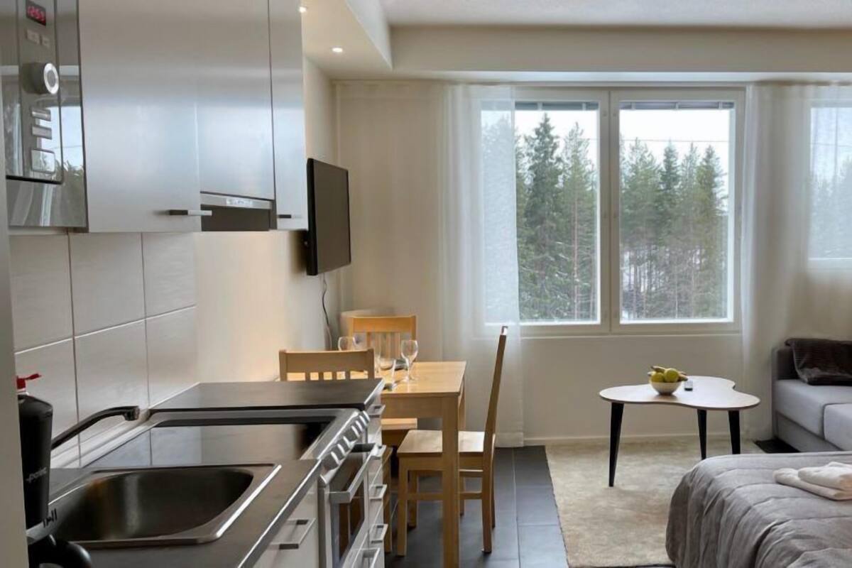 Una habitación de hotel moderna con kitchenette, una cama, un sofá y una pequeña mesa de comedor.