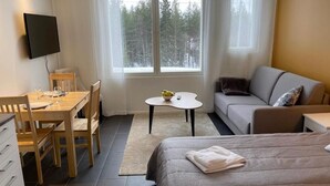 Habitación de hotel con cama, sofá, mesa de comedor con sillas, una mesita redonda con un bol y control remoto, y un televisor montado en la pared.