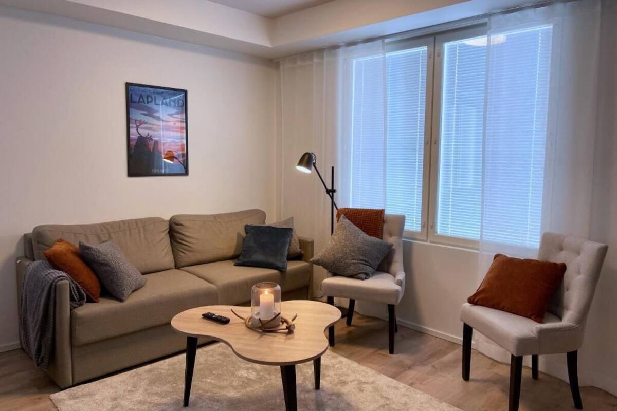 Una sala de estar con un sofá beige, un sillón blanco, una mesa de centro redonda y una lámpara de pie.