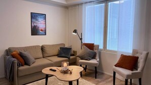 Una sala de estar con un sofá beige, un sillón blanco, una mesa de centro redonda y una lámpara de pie.