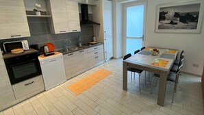Eine moderne Küche mit eingebauten Geräten, ein Essbereich mit Tisch und Stühlen sowie ein Blick ins Freie durch ein großes Fenster.