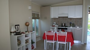A compact kitchen with white cabinets, a dining table with a red tablecloth, and a window with curtains. - Direttamente Sulla Spiaggia, Vista Lago Impareggiabile (Moniga del Garda)