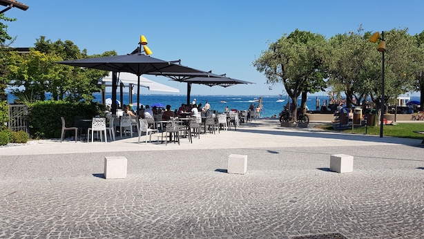 An outdoor seating area with tables and chairs, a covered pavilion, and a view of the sea. - Direttamente Sulla Spiaggia, Vista Lago Impareggiabile (Moniga del Garda)