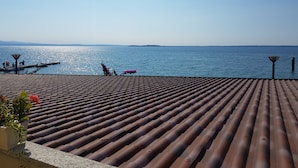 A tiled roof overlooking a calm sea with a distant shoreline. - Direttamente Sulla Spiaggia, Vista Lago Impareggiabile (Moniga del Garda)