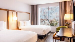 Habitación de hotel con dos camas, un escritorio, una silla y un ventanal con vistas a flores de cerezo.