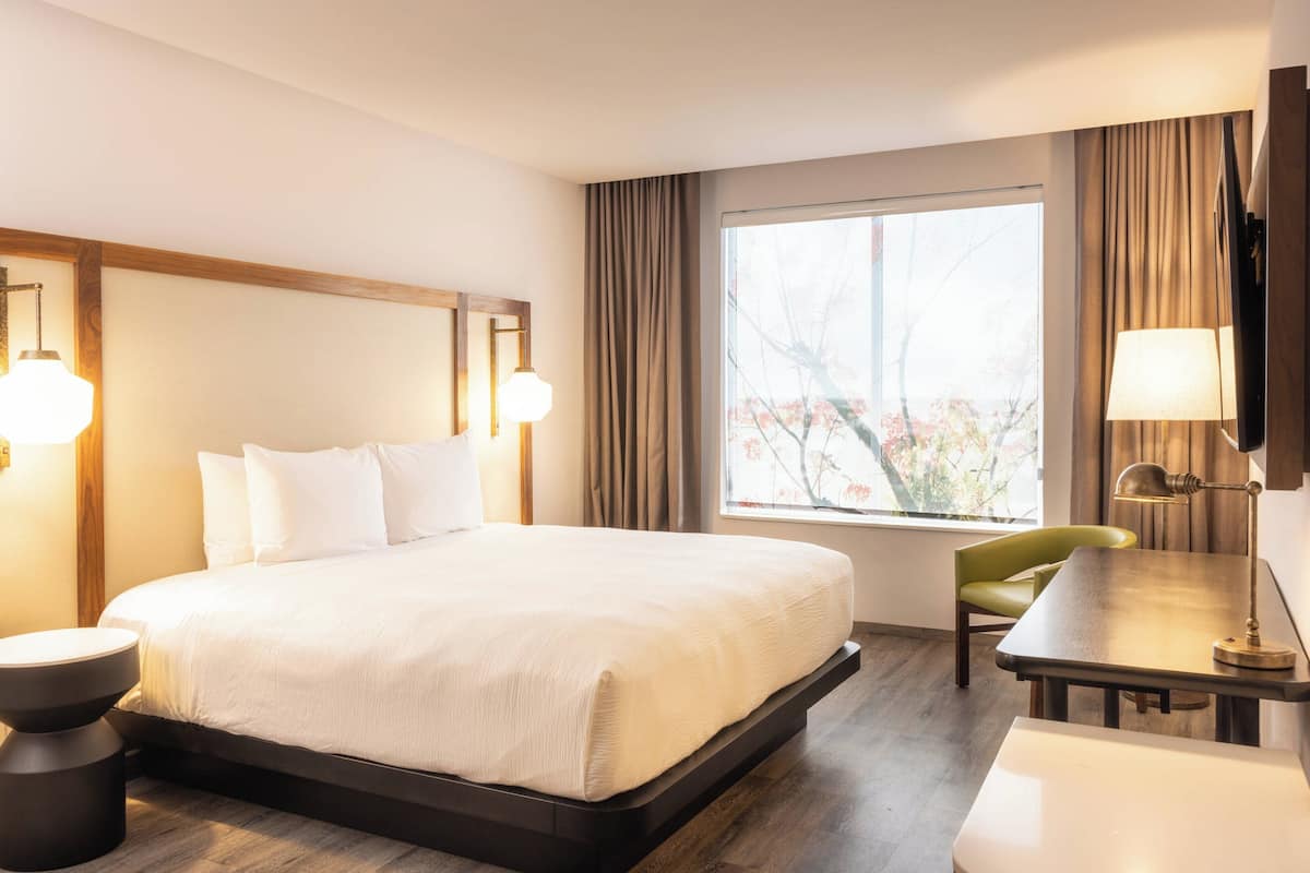 Hotellihuone, jossa on suuri sänky, työpöytä, tuoli ja ikkuna, jossa on verhot.