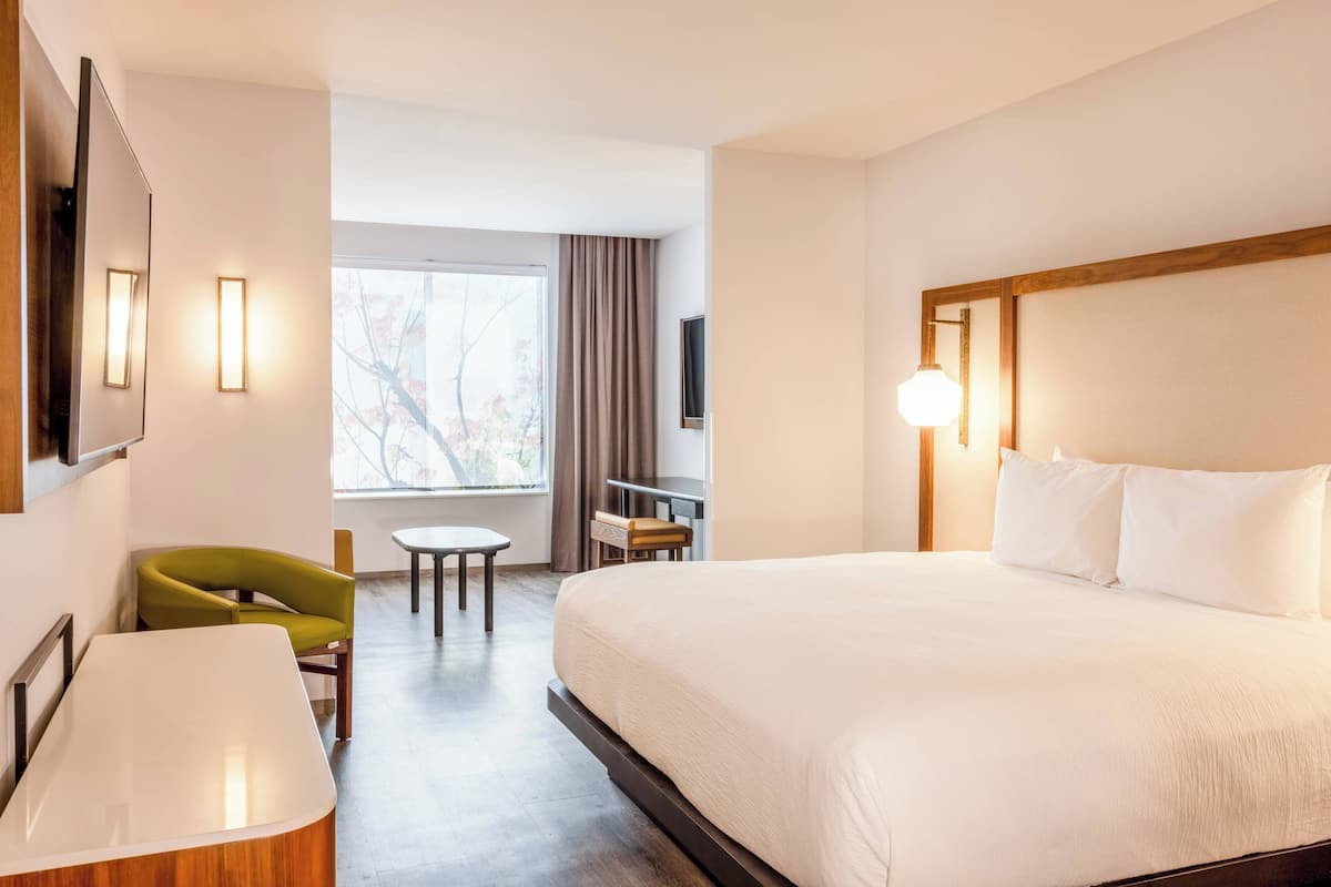 Hotellihuone, jossa on suuri sänky, työpöytä, tuoli, televisio ja ikkuna, jossa on verhot.