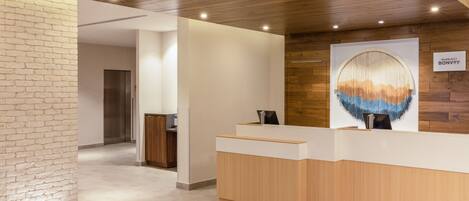 A reception area with a wooden reception desk, a large abstract wall art piece, and a sign indicating the hotel name 'Marriott Bonvoy'.