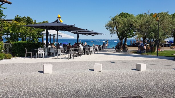 An outdoor seating area with tables and chairs, a covered pavilion, and a view of the sea. - Direttamente Sulla Spiaggia con Terrazza Vista Lago (Moniga del Garda)