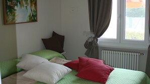 A bedroom with a bed, green bedding, a window with curtains, a radiator, and a painting on the wall. - Direttamente Sulla Spiaggia con Terrazza Vista Lago (Moniga del Garda)