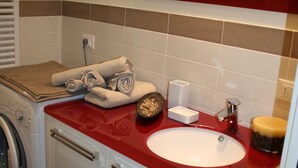 A bathroom with a red countertop, a white sink, a mirror, a towel rack, and a washing machine. - Direttamente Sulla Spiaggia con Terrazza Vista Lago (Moniga del Garda)