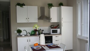 A compact kitchen with white cabinets, a microwave, and a sink. There are two chairs and a table with plates and a vase of flowers. - Direttamente Sulla Spiaggia con Terrazza Vista Lago (Moniga del Garda)