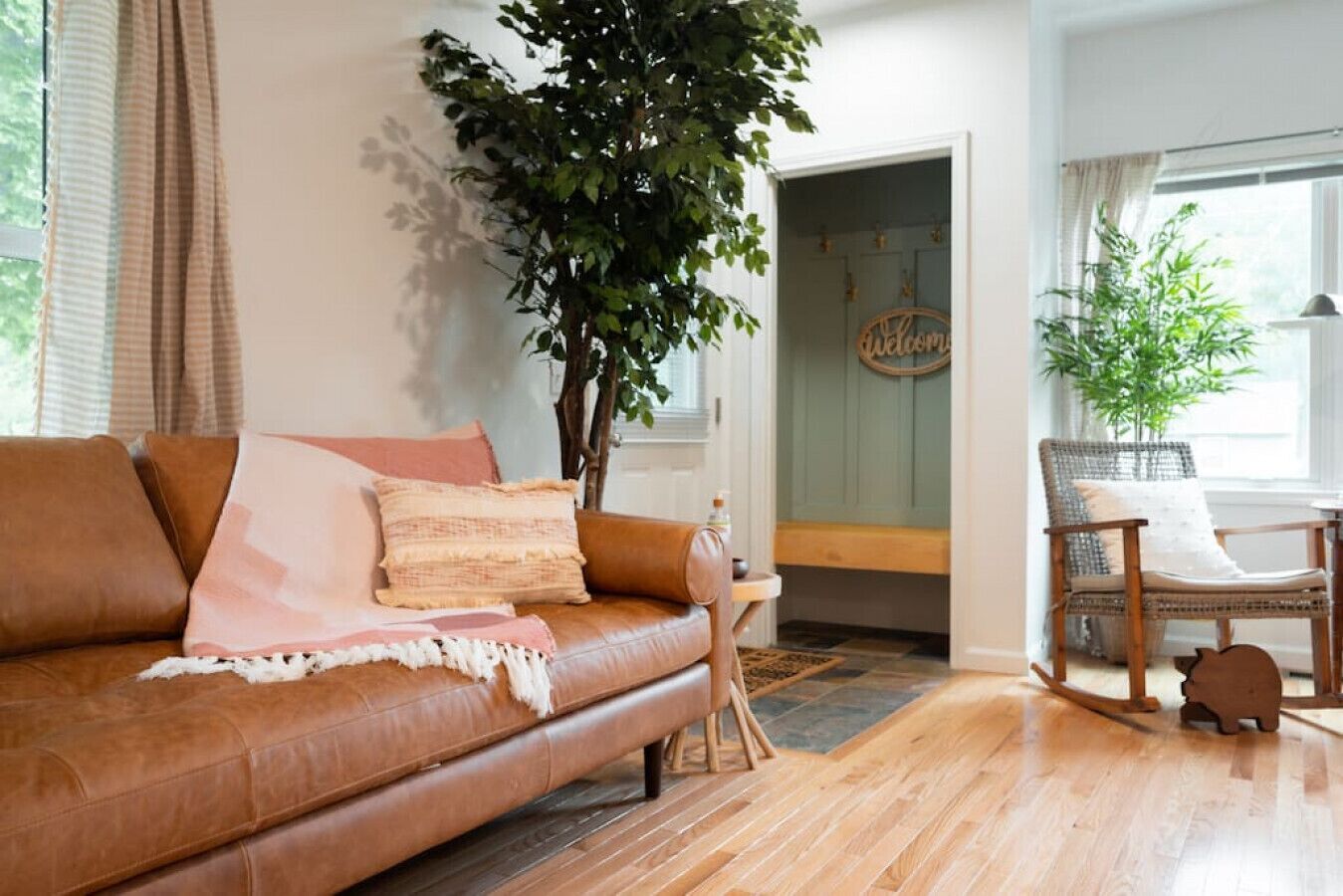 A cozy living room with a brown leather sofa, a large green plant, and a wicker chair.