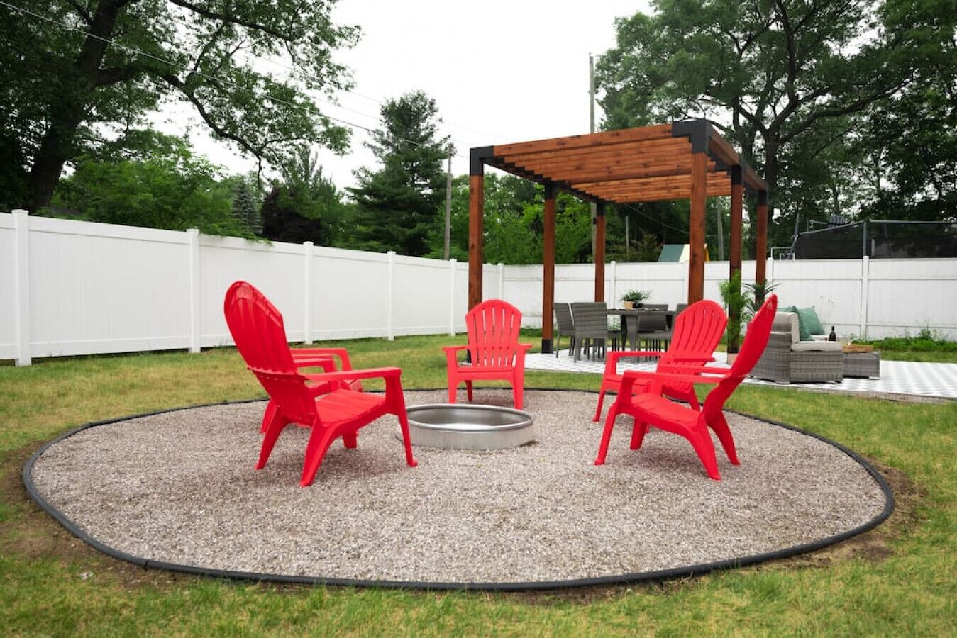 A circular outdoor seating area with red chairs, a fire pit, and a wooden pergola.