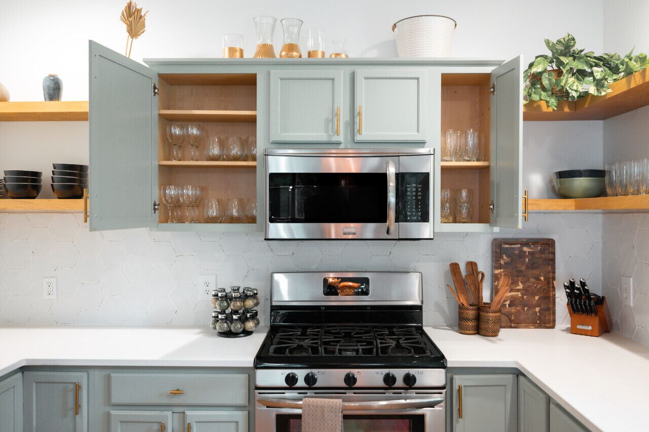 Una cocina equipada con estufa, horno, microondas y alacenas abiertas.