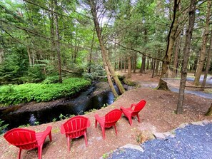 A forested area with a small stream, red chairs, and a hammock.