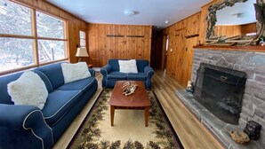 A cozy living room with wooden walls, two blue sofas with white cushions, a wooden coffee table, and a fireplace.
