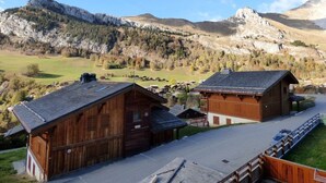 Une cabane en bois, dotée d’un toit en pente, située dans une région montagneuse et offrant une vue sur une vallée et des sommets lointains.