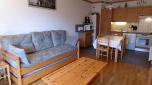Un espace de vie compact comprenant un canapé, une table en bois, un coin cuisine et un espace repas.