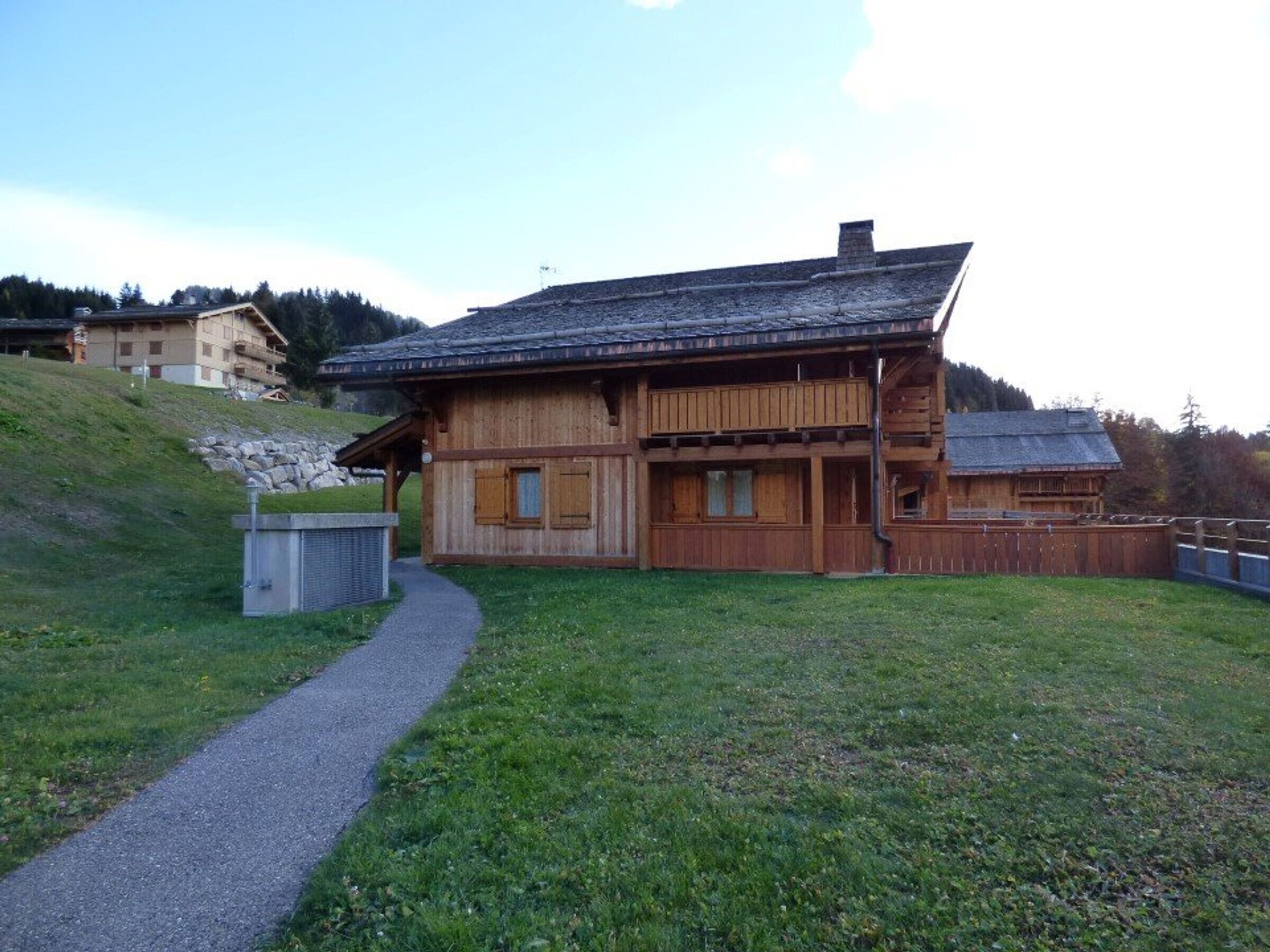A wooden chalet with a sloped roof, a covered porch, and a gravel path leading to the entrance.
