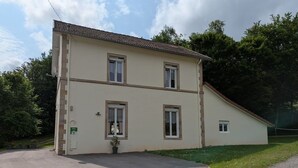 A two-story building with a sloped roof, a front entrance with a potted plant, and a small porch area. - Charming Countryside Retreat with Modern Comforts near Hiking Trails and Lakes (Uriménil)