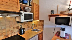 A compact kitchen with a microwave, kettle, sink, and a small television. - Comfortable 40m² apartment for 6 near ski slopes, large terrace (Le Grand-Bornand)