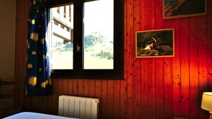 A room with a bed, a window with curtains, a radiator, and a picture on the wall. - Comfortable 40m² apartment for 6 near ski slopes, large terrace (Le Grand-Bornand)