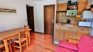 A compact living space with a wooden dining table, chairs, a kitchenette with a microwave, and a red polka-dotted sofa. - Comfortable 40m² apartment for 6 near ski slopes, large terrace (Le Grand-Bornand)