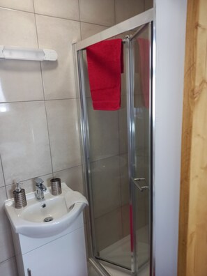A bathroom with a glass shower enclosure, a white sink with a mirror, and a red towel hanging on the shower door. - Country Cottage Apartment, Valentia Island, Kerry (Valentia Island)